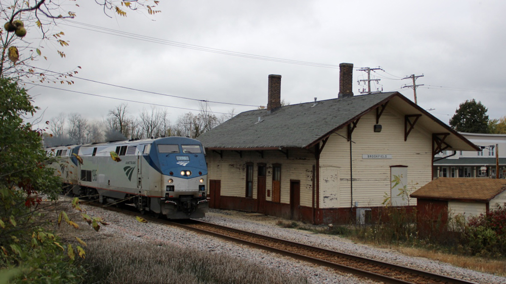 Passenger train passing one-story wooden station