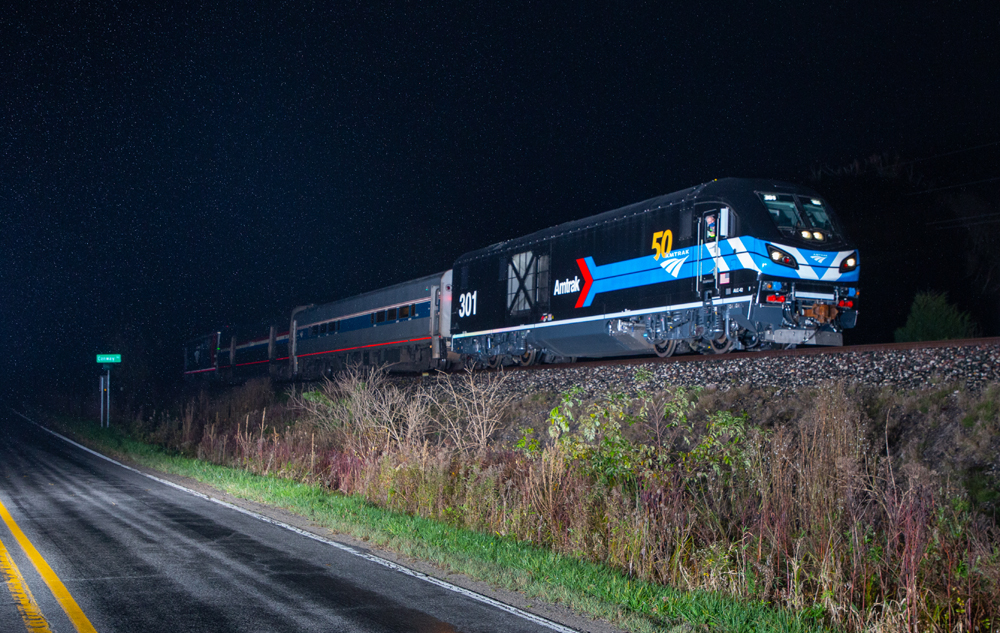Black locomotive with blue stripes leads short train at night
