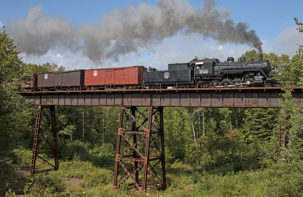 Steam locomotive pulling freight cars over bridge