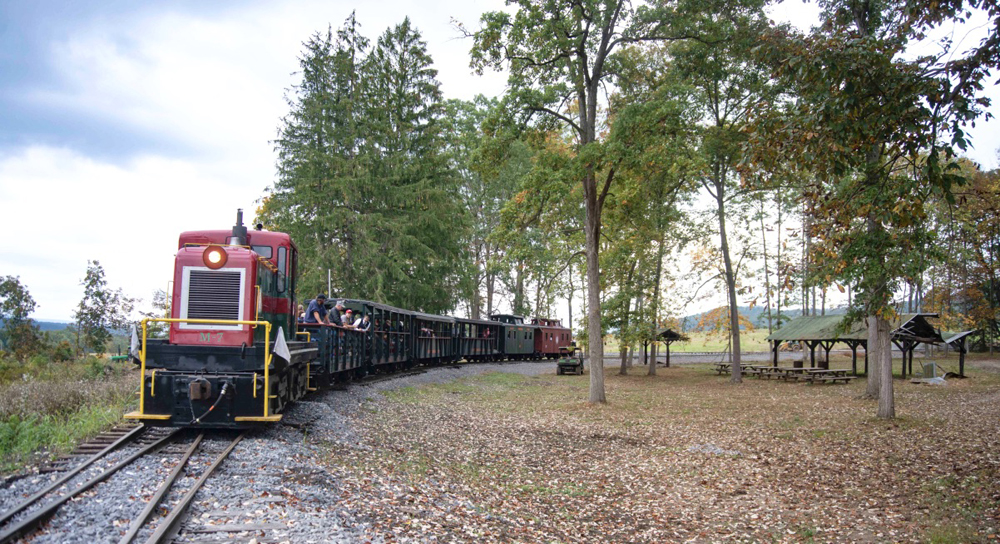 Train of open cars and cabooses pulled by red and green center cab diesel