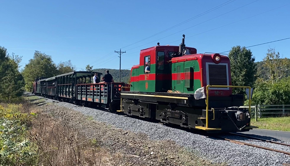 Red and green diesel pulling open-air cars for passengers