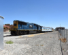 Blue and yellow locomotive shoves passenger cars on a rail siding.