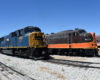 A homely looking blue-and-yellow locomotive stands to the left of a chocolate-brown and orange cab locomotive.