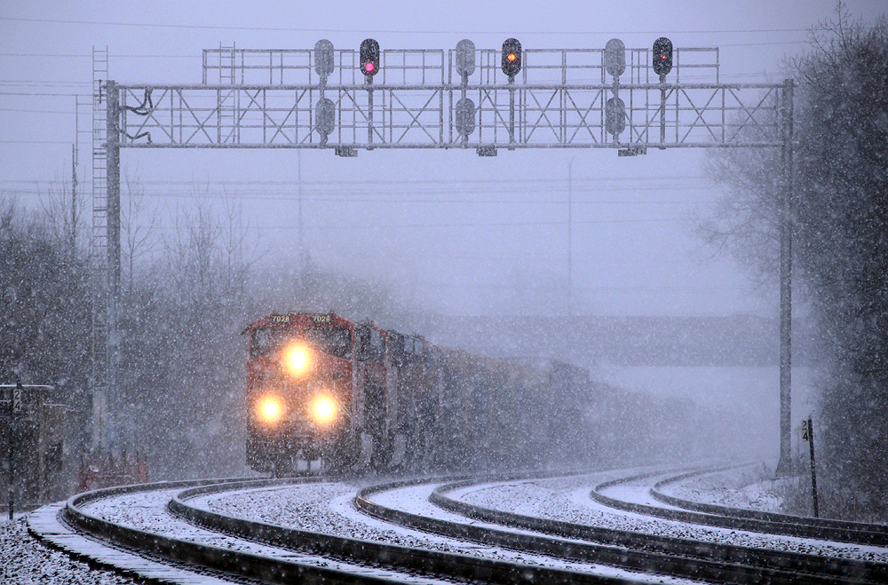 Chicago Railfanning at Lisle: Orange locomotives moving train in heavy snow.