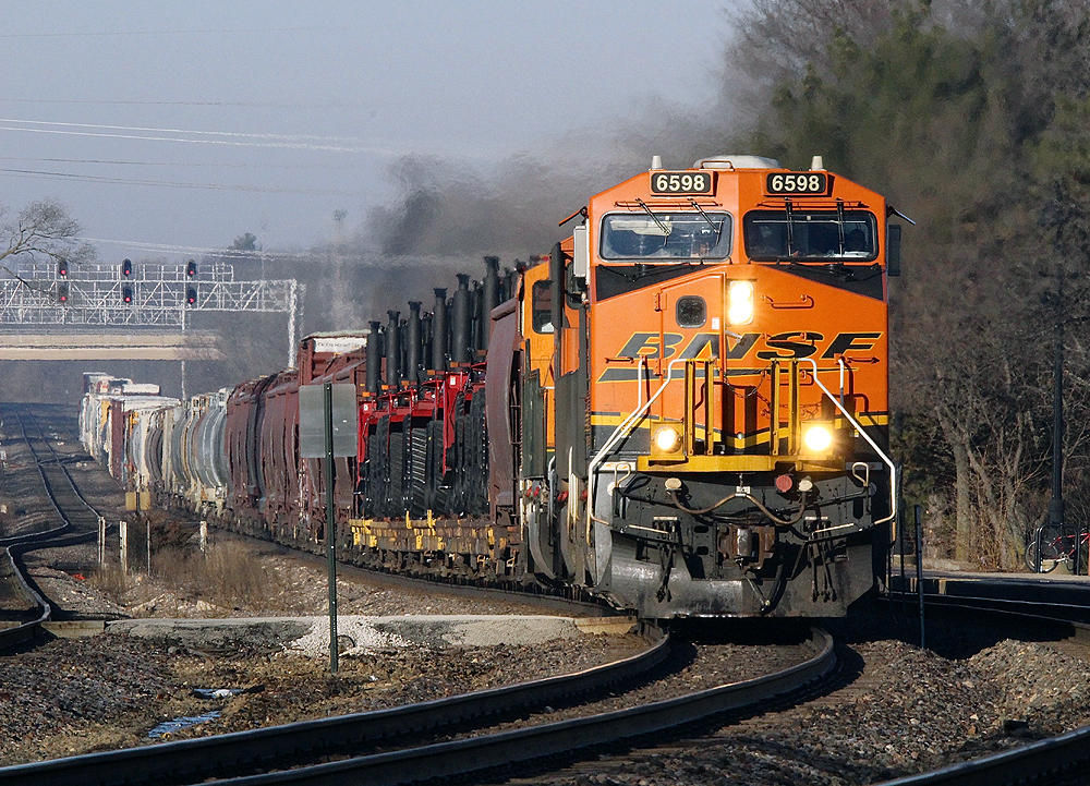 Orange locomotives approaches curve with train stretched out behind on long straight.