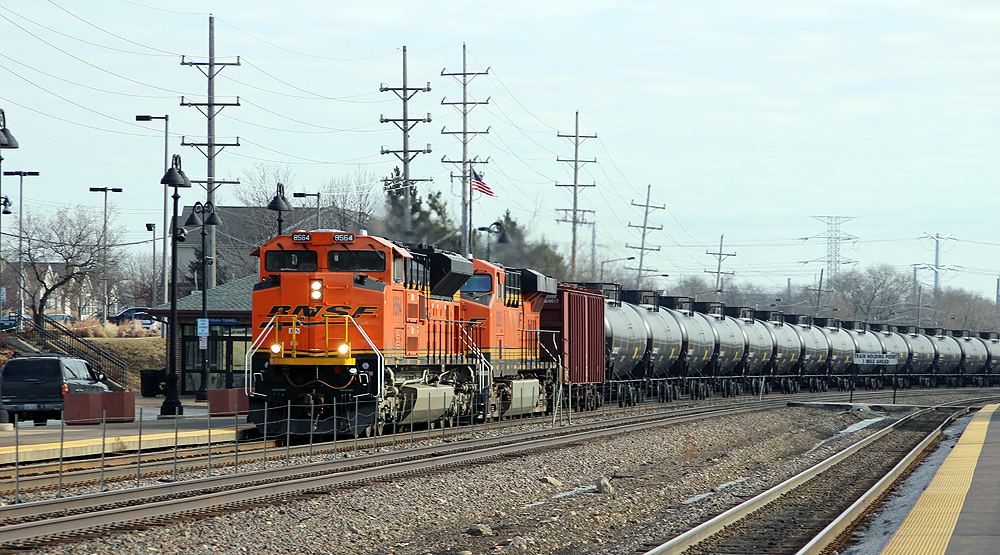 Train with two orange locomotives and tank cars rounds curve.