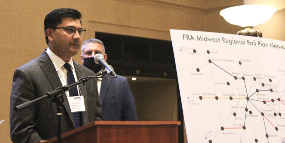 Man at podium, speaking next to rail map