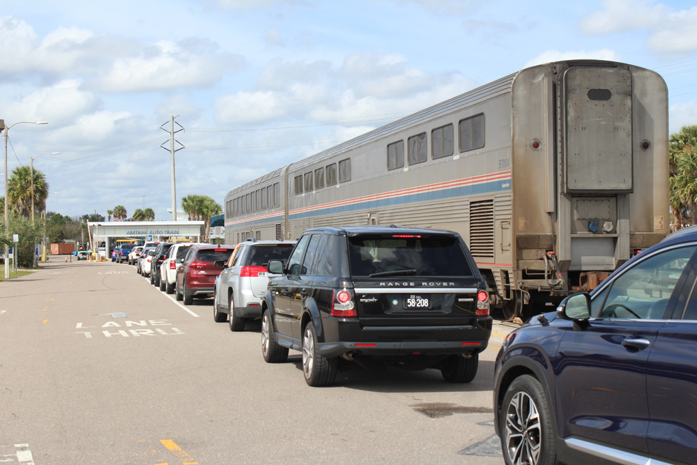 Cars lined up on road next to passenger train