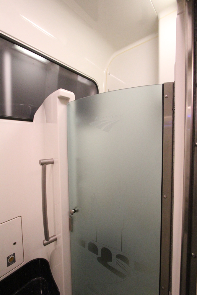 Shower on train with pale pink walls and smoked glass door.