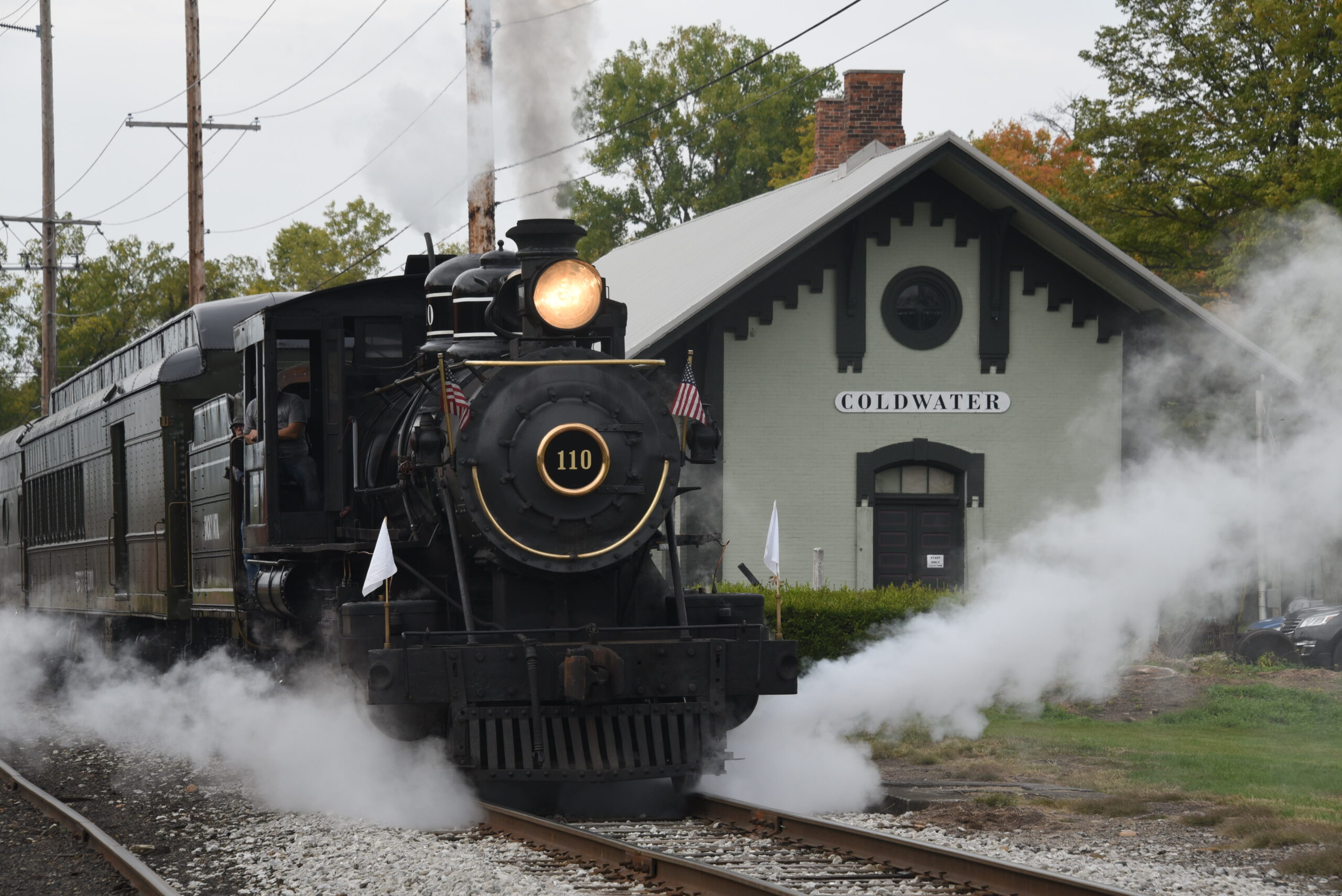 Small black steam locomotive departs train station.