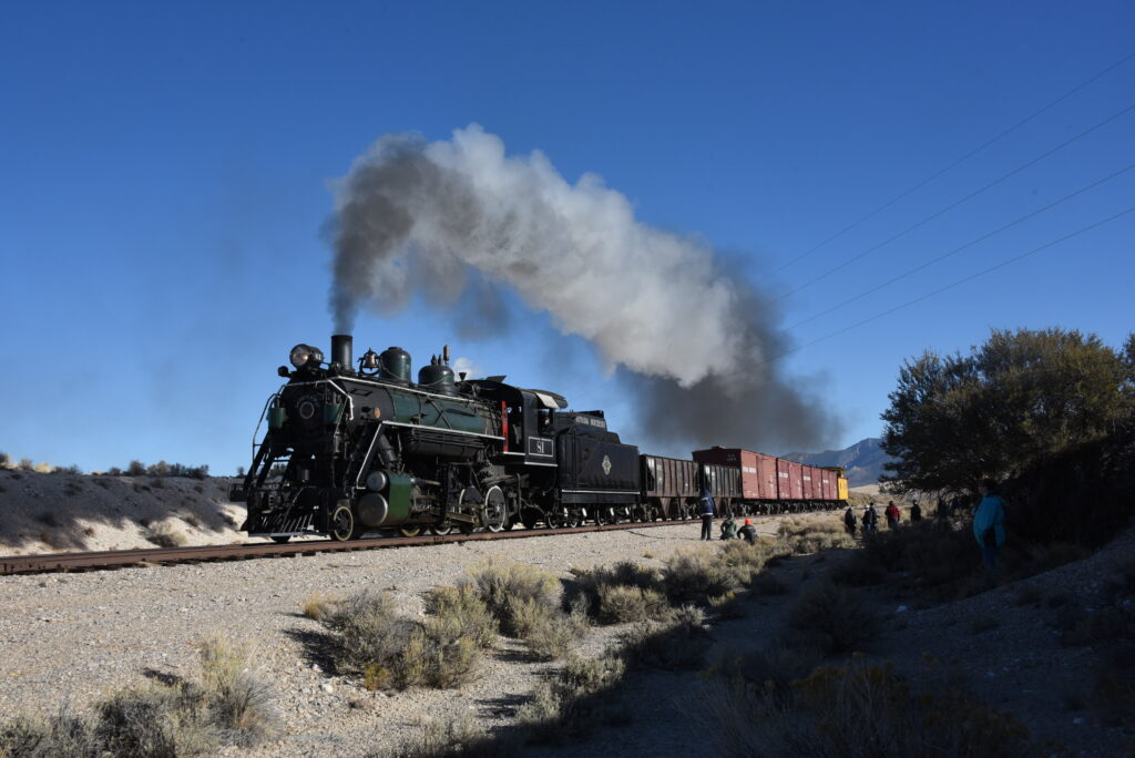 Steam locomotive at speed with tall plume of smoke.