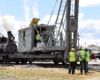 Operating railroad pile driver with crews looking on.