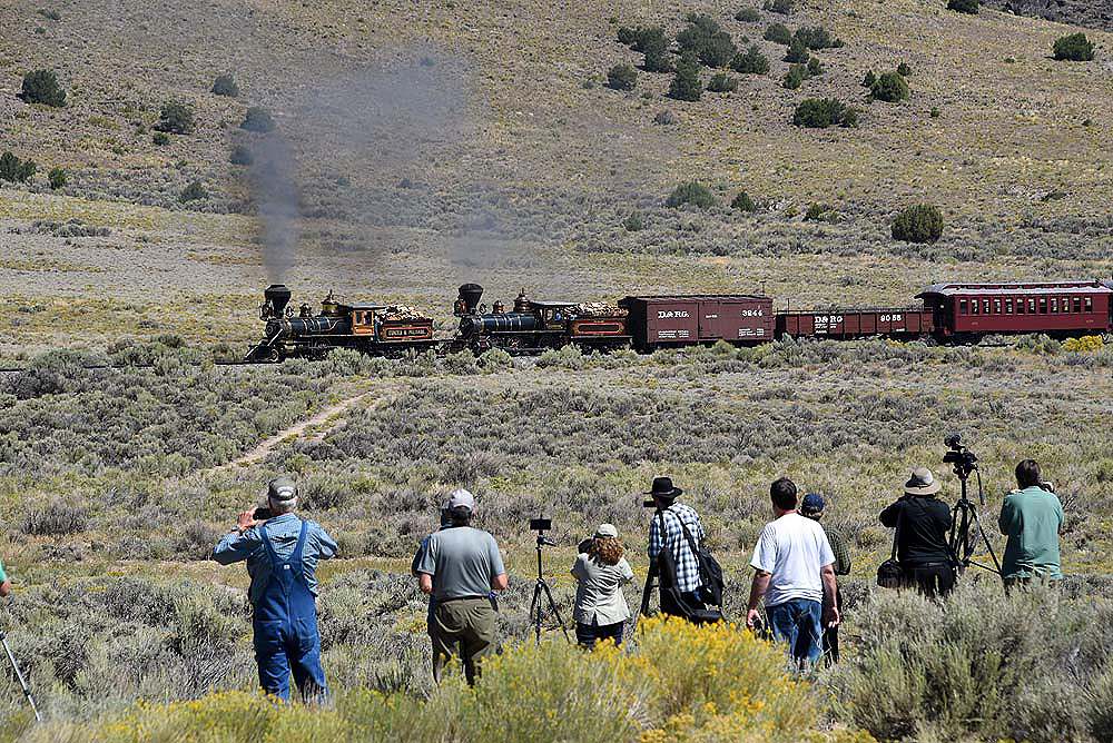 Steam hauled passenger train in open grassland.
