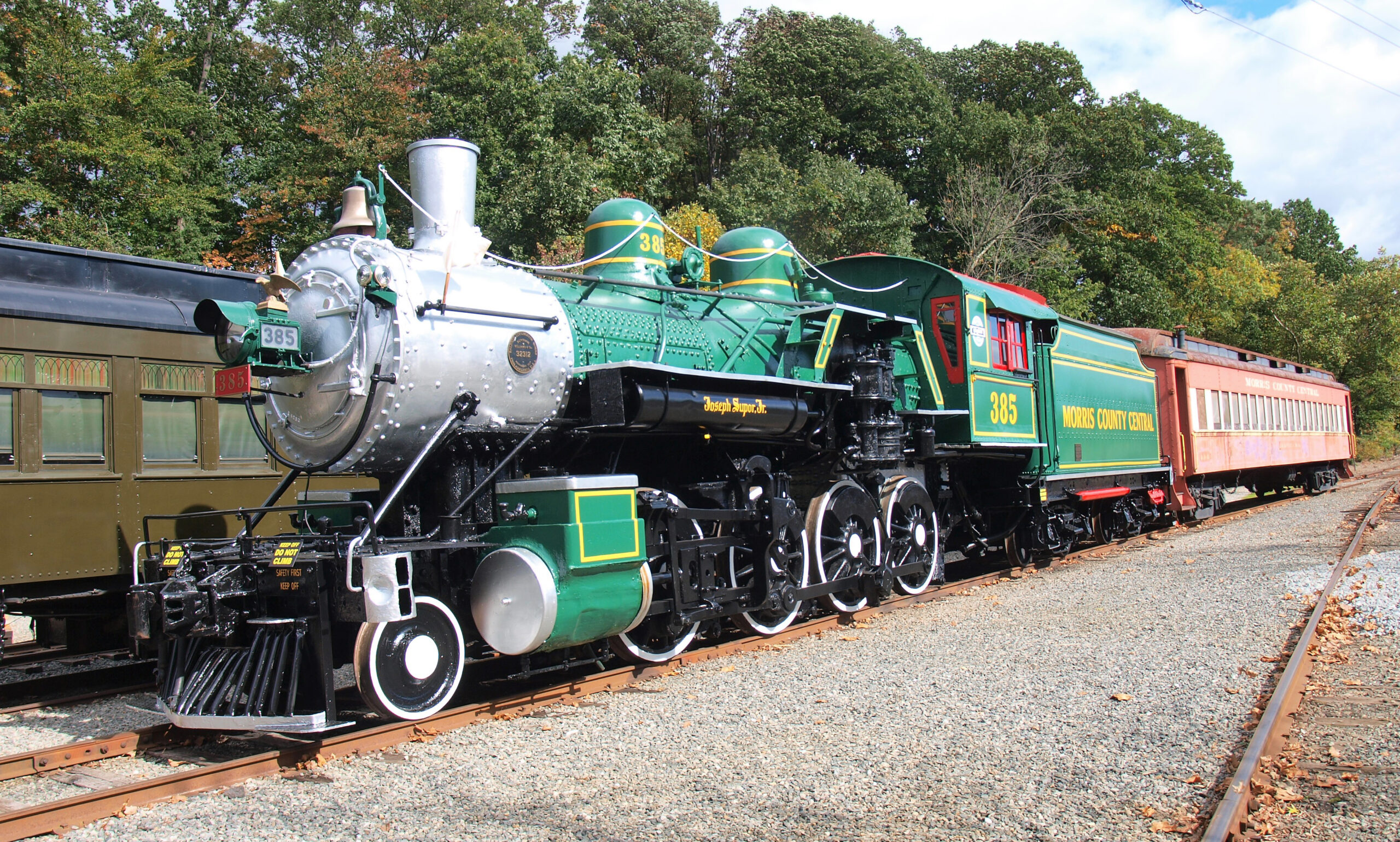 Steam locomotive with green and gold paint coupled to heavyweight passenger car