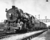 Steam locomotive pulls freight train under signal bridge and across diamond