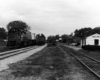 Two diesel-powered freight trains appear side-by-side on double track in front of station