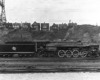Broadside of clean steam locomotive in valley in front of row of houses