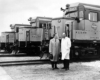 Men in long jackets on holding a hat stand in front of new diesel locomotive noses lined up