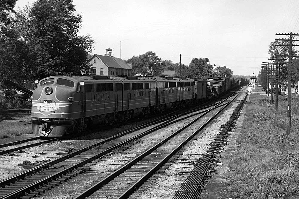 Streamlined diesel locomotives bring a freight train through town on a multiple track line
