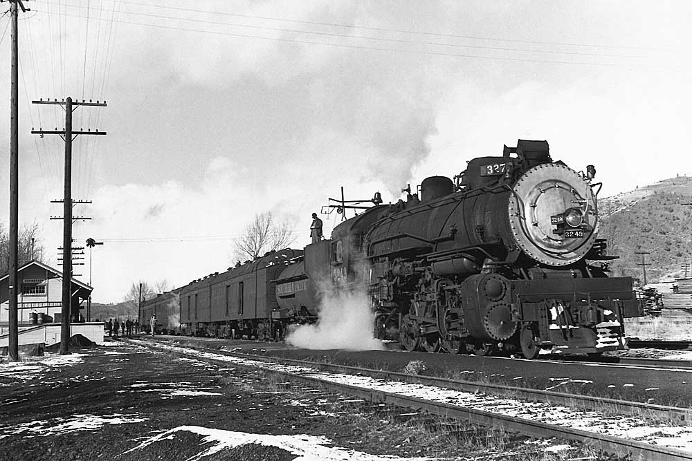 Man stands on steam locomotive tender in front of station in snow