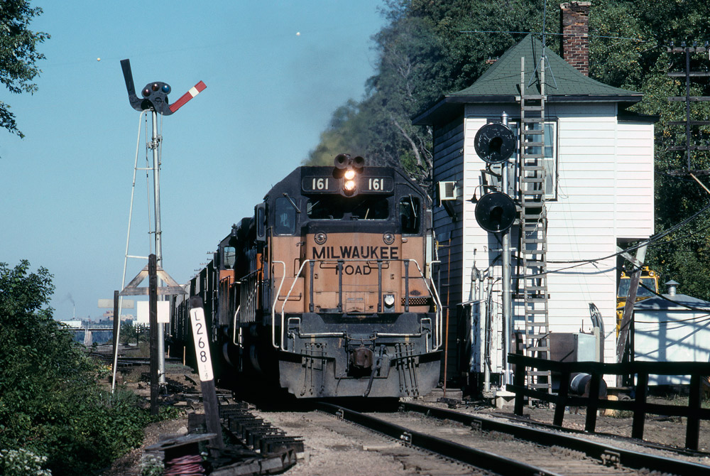 Color head-on photo of road-switcher diesel locomotive passing signal tower
