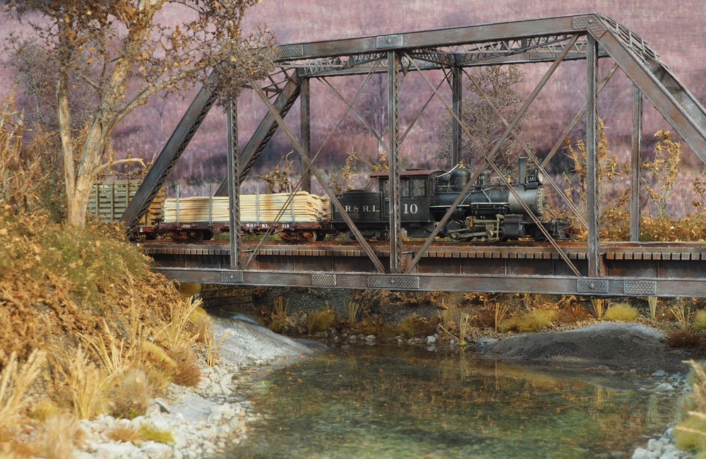 A geared steam locomotive drives a wooden train on a steel trestle above a stream