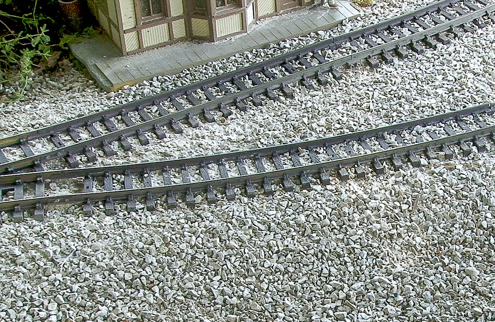 Large-scale track is seen resting in a bed of gravel in front of a small wood depot