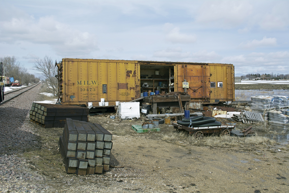 Weathered yellow steel insulated boxcar with railroad ties, pallets, and other debris piled in front