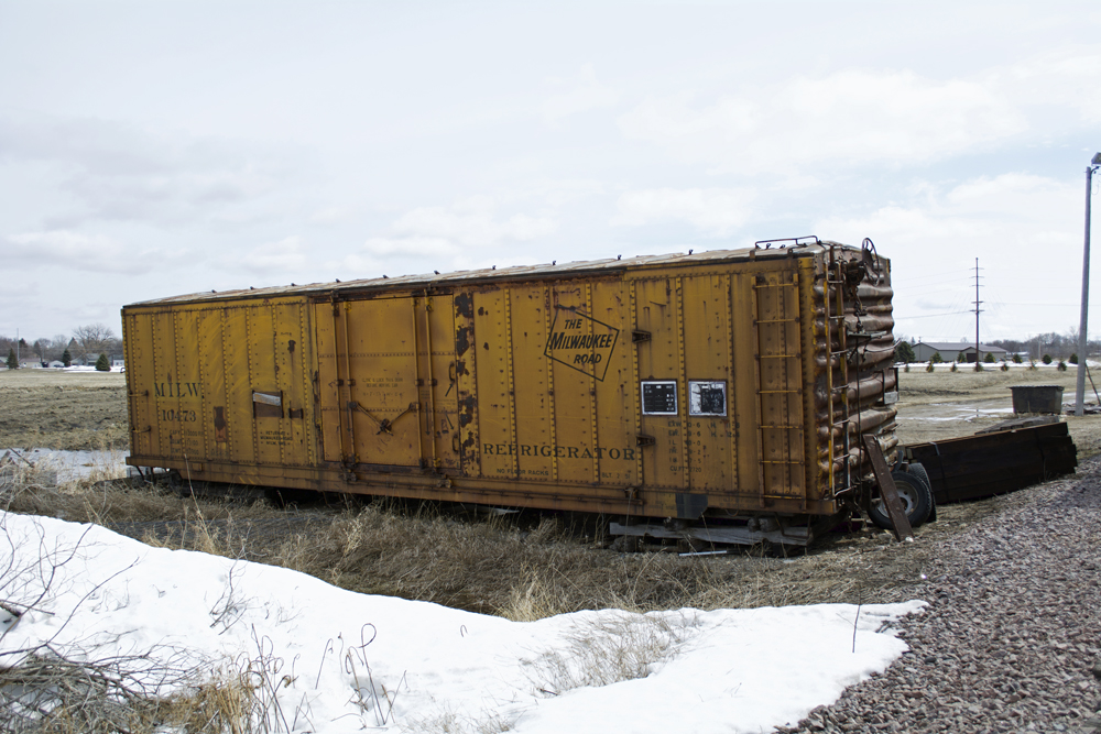 Left-side view of Milwaukee Road insulated boxcar number 10473 sitting off the rails with a snowdrift in front
