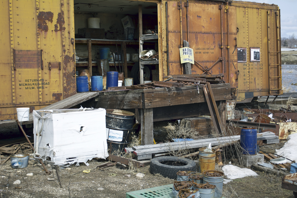 Assorted railroad supplies stored on shelves inside a boxcar and scattered around in front of it