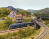 A train passes under a siding bridge, houses sit in the background