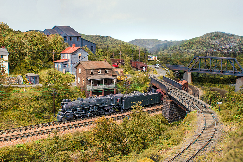 A train passes under a siding bridge, houses sit in the background