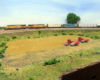 A yellow Union Pacific locomotive-led train passes a field with red farm equipment in N Scale.