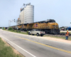 Two Union Pacific locomotives lead a train near a grain elevator.