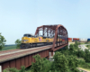 Two Union Pacific locomotives lead an intermodal train over a steel truss bridge on a verdant HO scale layout.