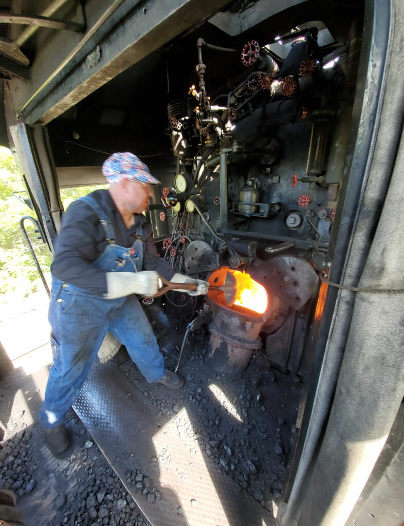 View from behind fireman tossing coal into firebox in steam engine on a Frisco steam locomotive cab ride