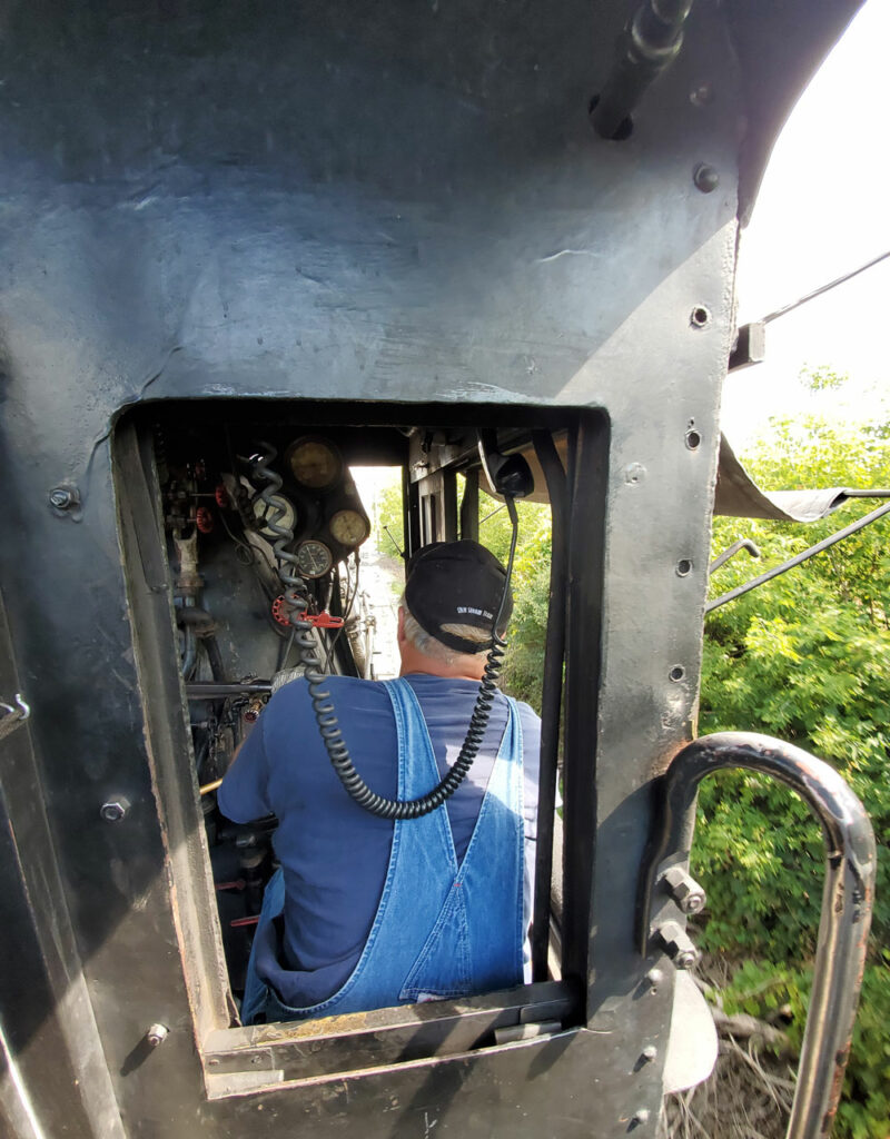 view from behind steam engineer in baseball cap at throttle 