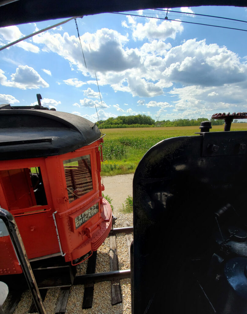 streetcar and passengers pass on adjacent track to steam passenger train