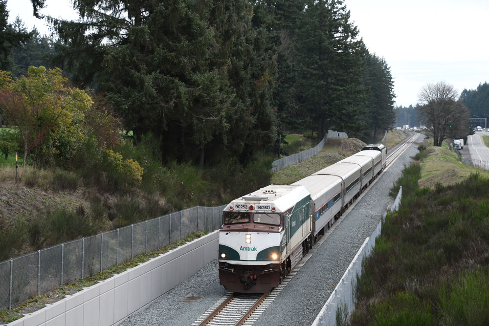 White passenger locomotive leads white passenger cars on gray day