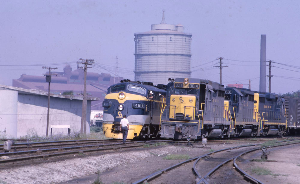 two yellow and blue locomotives next to each other on tracks with silo in background