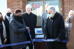 Woman cuts ribbon with large scissors while others watch