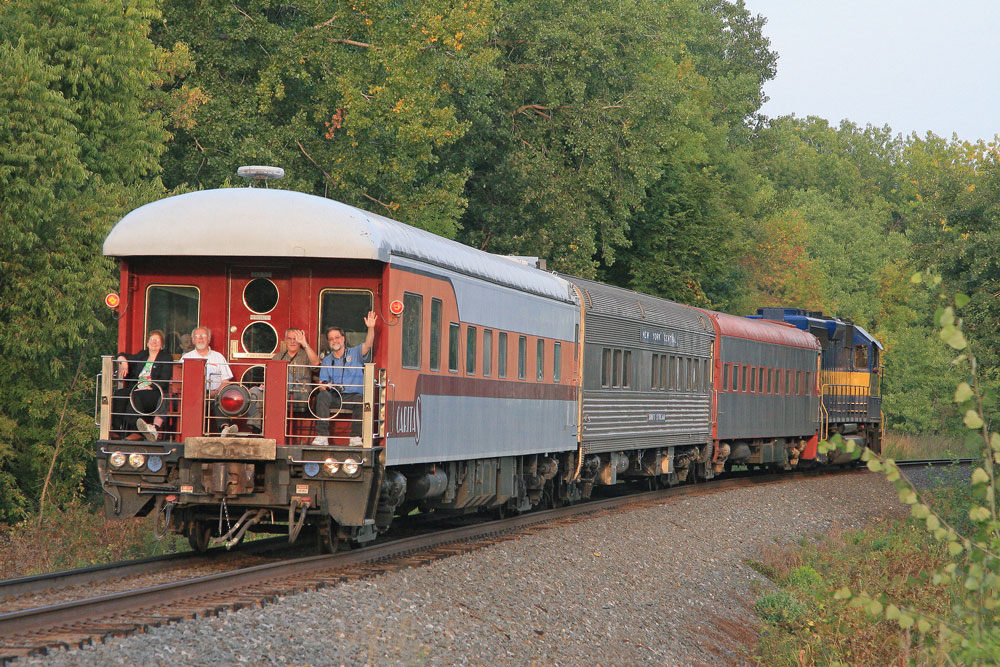 rear of train with orange passenger car with people seated on the rear