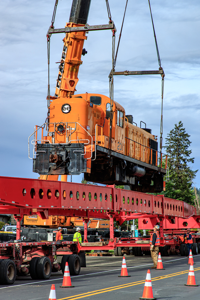 Orange locomotive above many-wheeled transport trailer