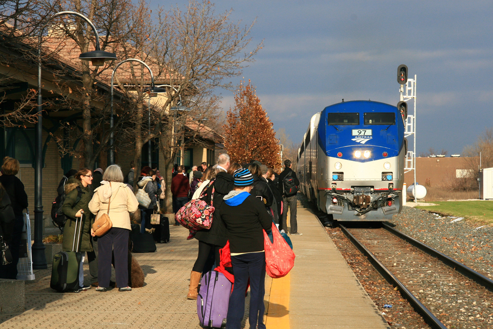 Passenger train arrives at station with large crowd waiting on platform