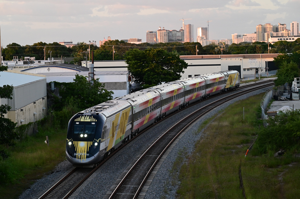 Passenger train on curve with city skyline in background