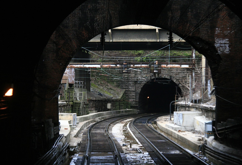 Two railroad tracks exiting one tunnel and entering another
