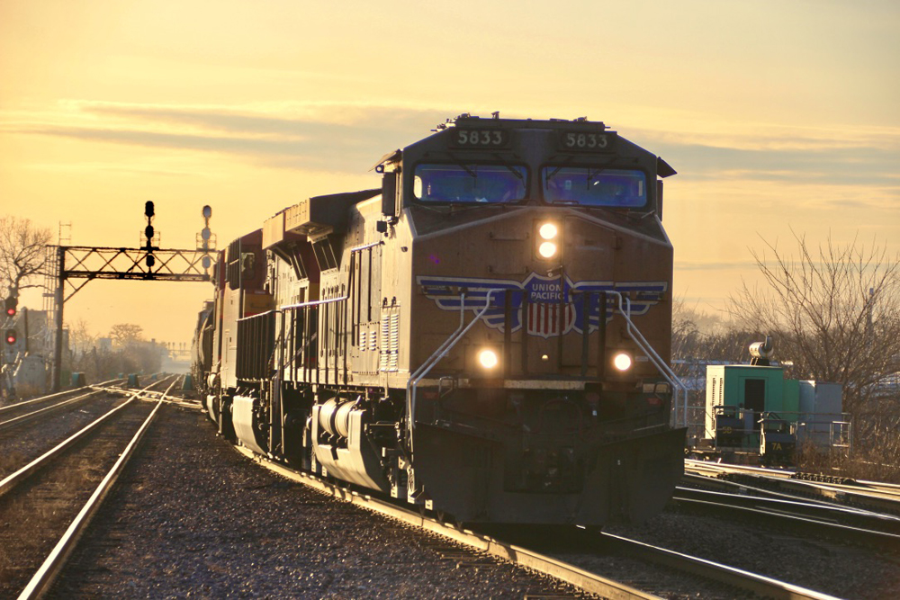 Locomotives lead freight train under golden sky from setting sun