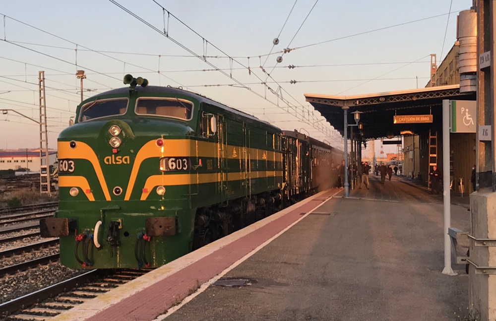 Green and gold streamlined locomotive at station