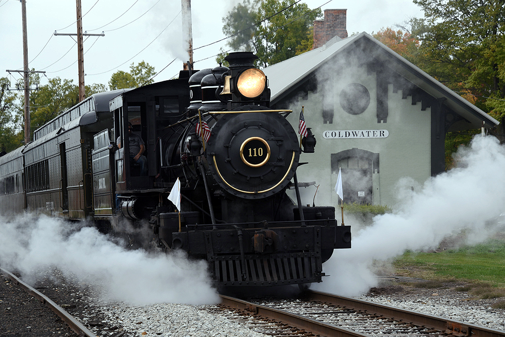 Black locomotive with heavyweight passenger cars passing station building