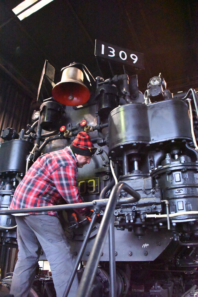 Man in flannel shirt and knit cap working at front of steam locomotive